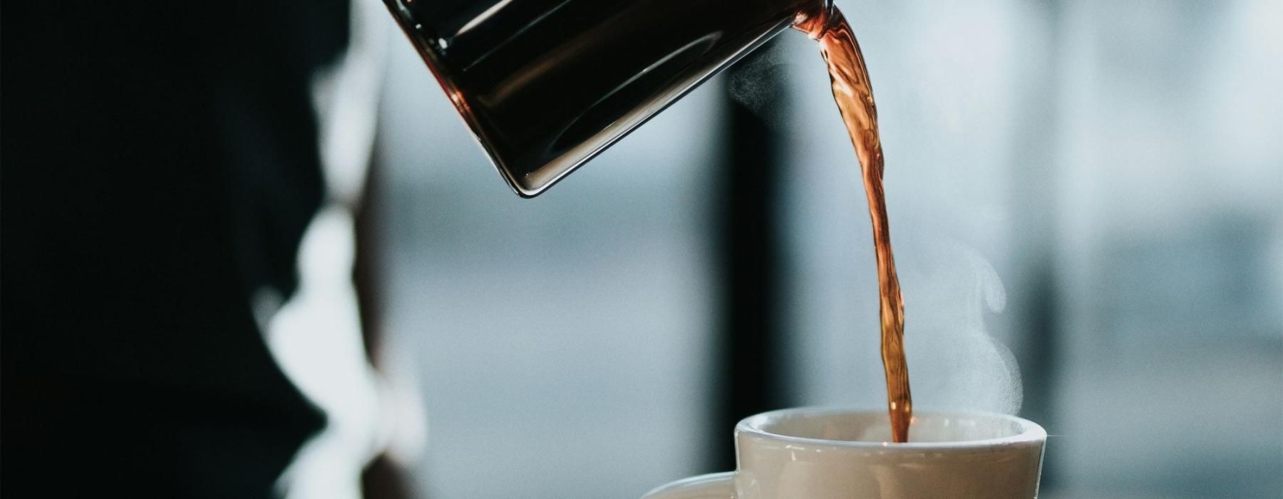 a person pouring a carafe of coffee into a cup